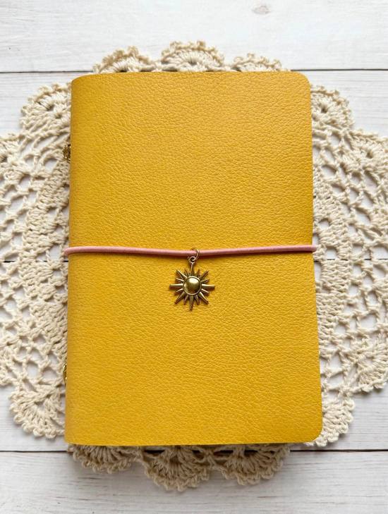 yellow leather journal with pink elastic cord and gold sun charm